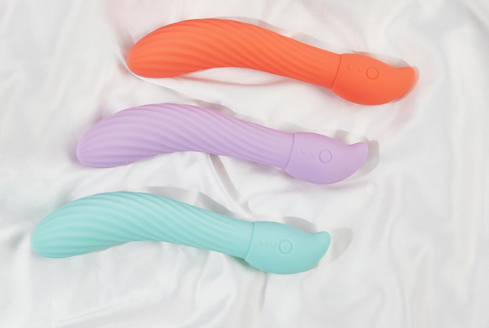 Three colorful air-suction vibrators arranged on white fabric, highlighting their smooth texture and design