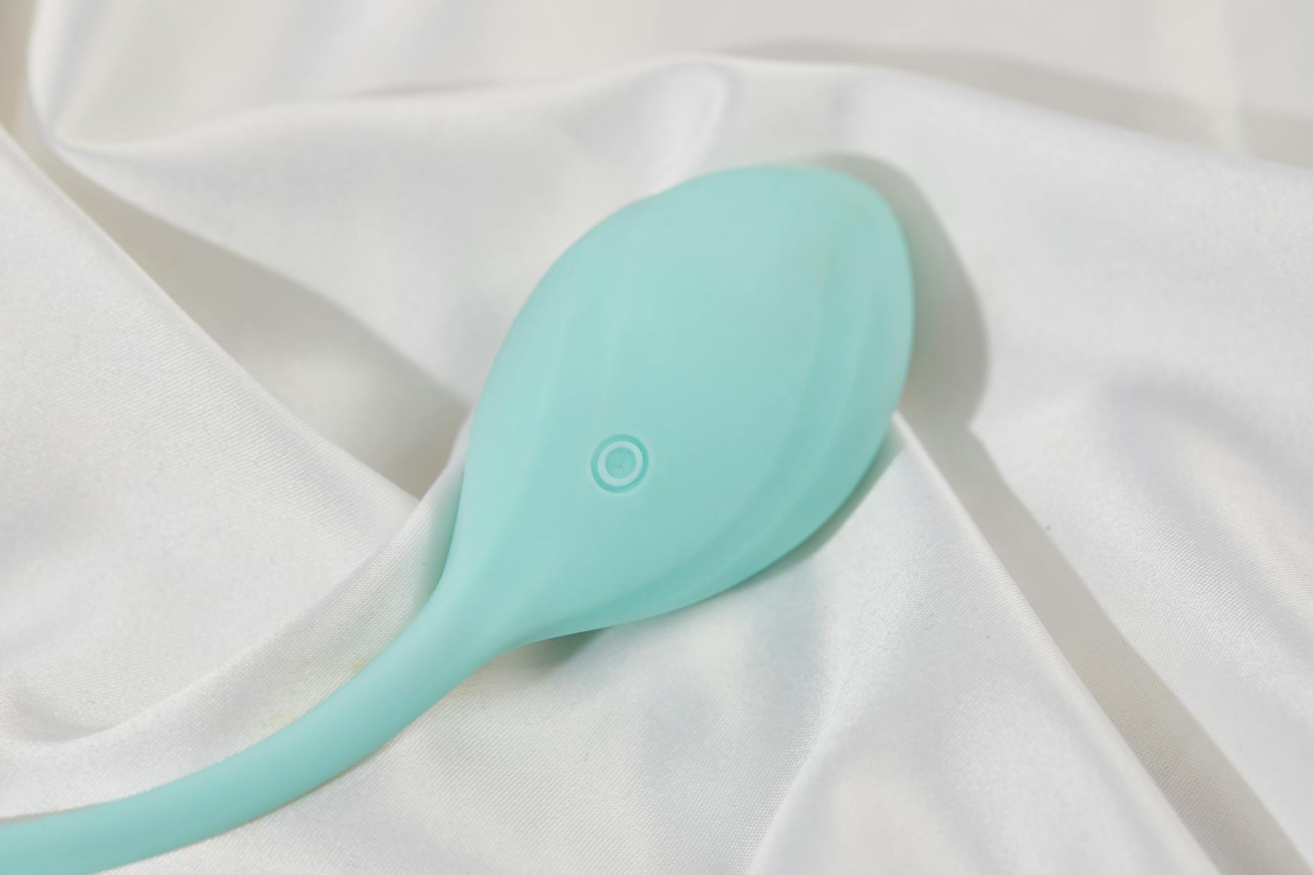 A teal clitoral vibrator on smooth white silk, representing modern tools for restoring intimate sensation