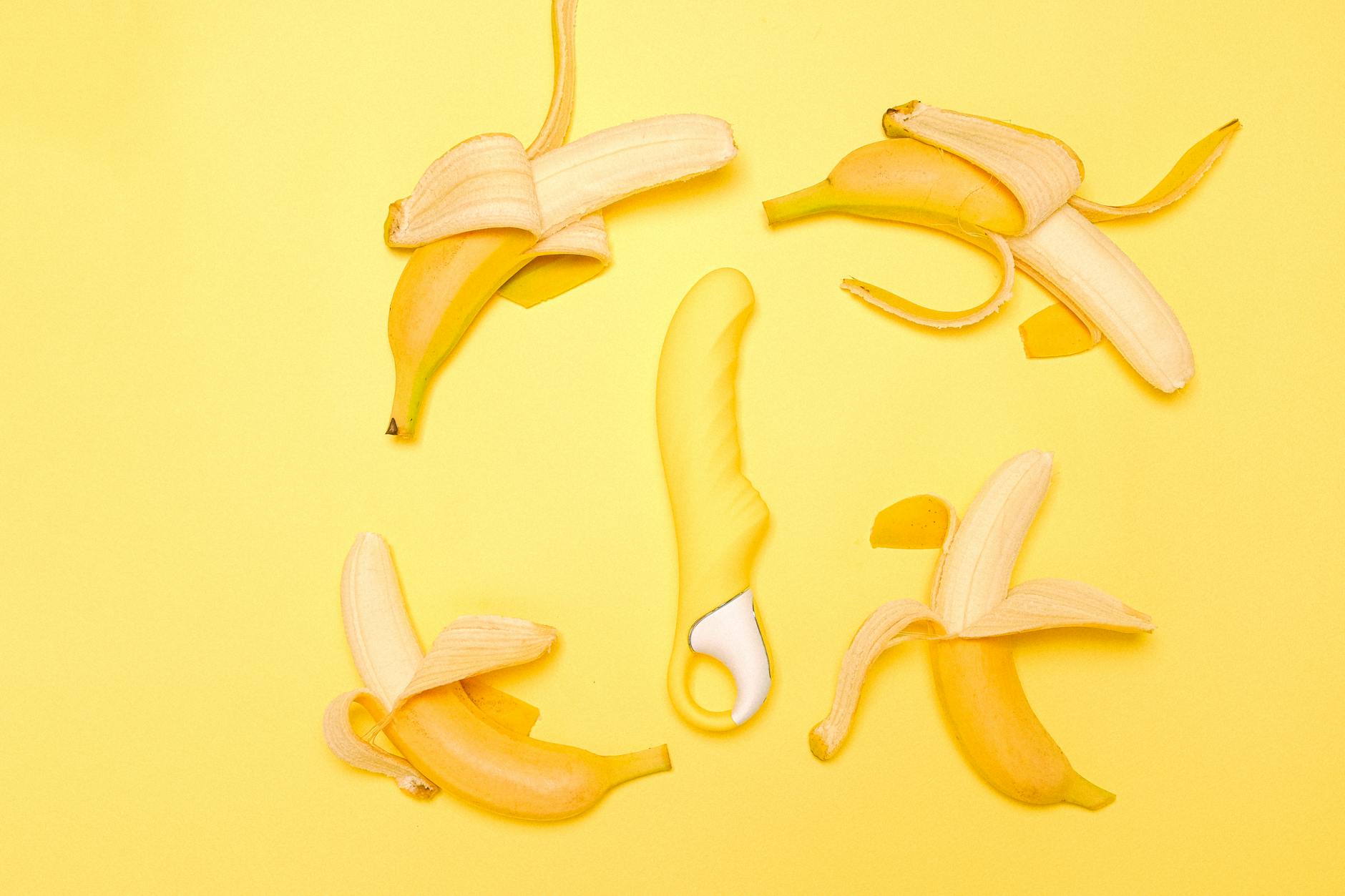 A yellow silicone lemon vibrator surrounded by fresh lemons on a bright yellow surface.