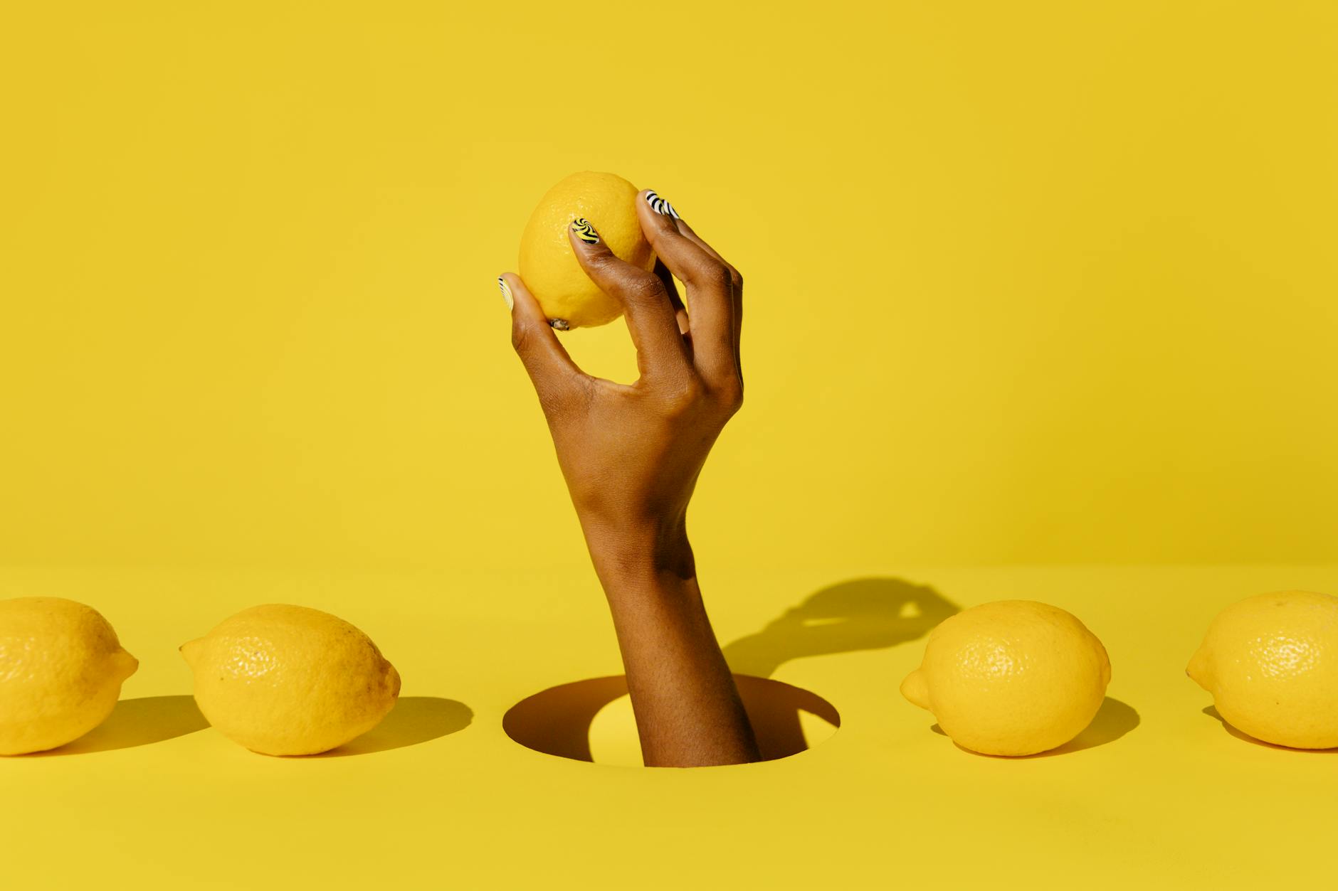 Hand holding a fresh lemon against a bright yellow background, symbolizing vitality and renewed pleasure