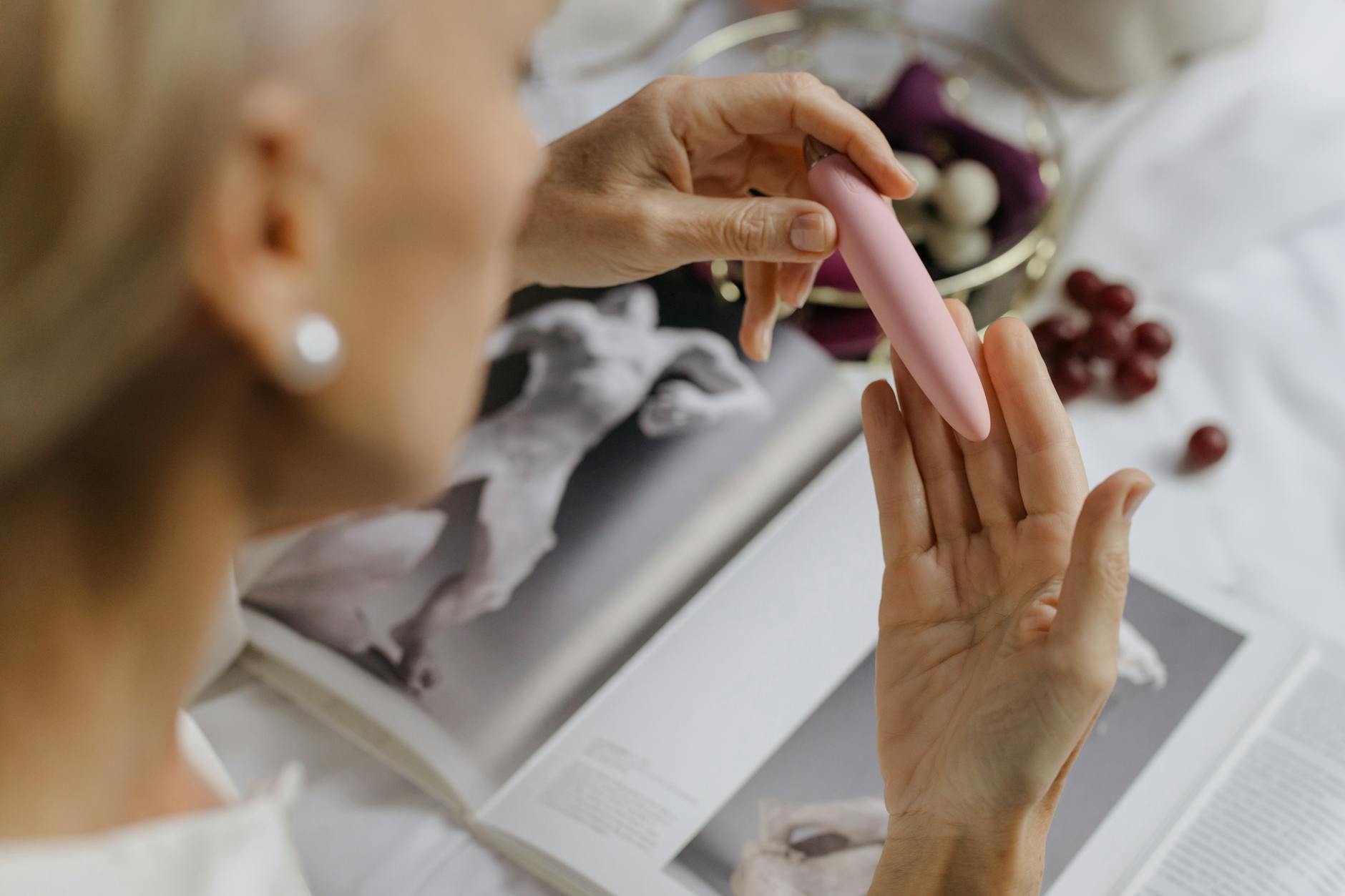 Woman holding a pink clitoral vibrator near art books, showing intimate comfort and personal choice