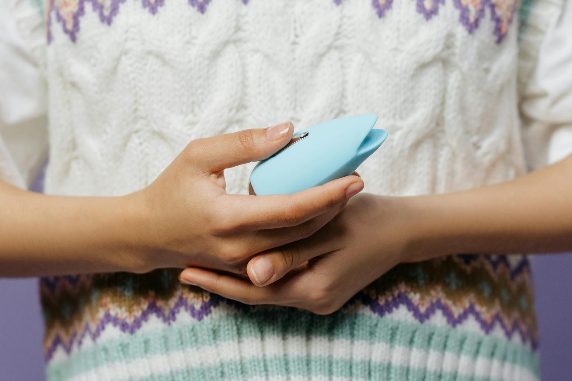 Close-up of hands holding a lemon clitoral vibrator against a textured sweater