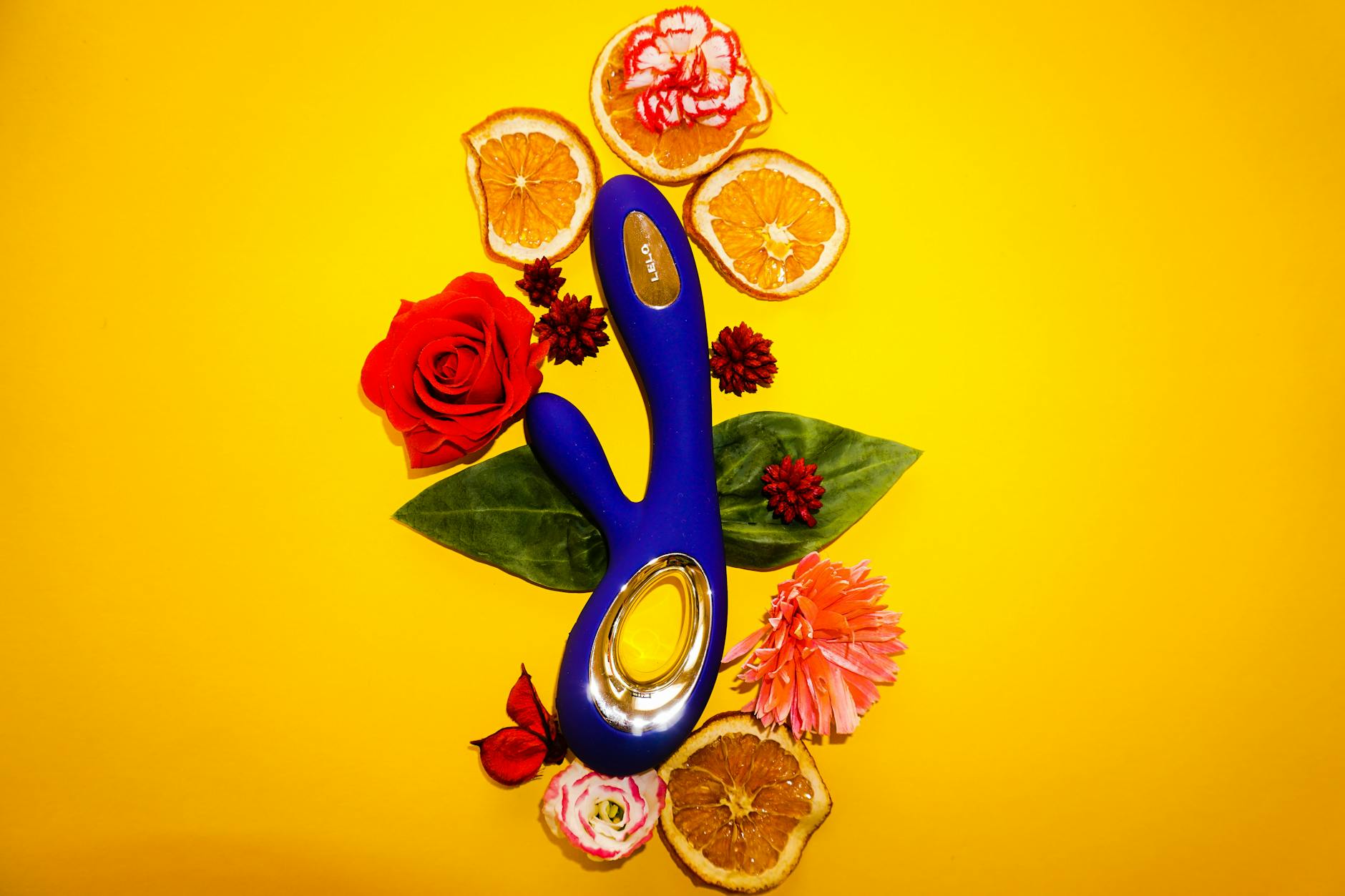 A blue lemon vibrator surrounded by flowers and citrus on a bright yellow background