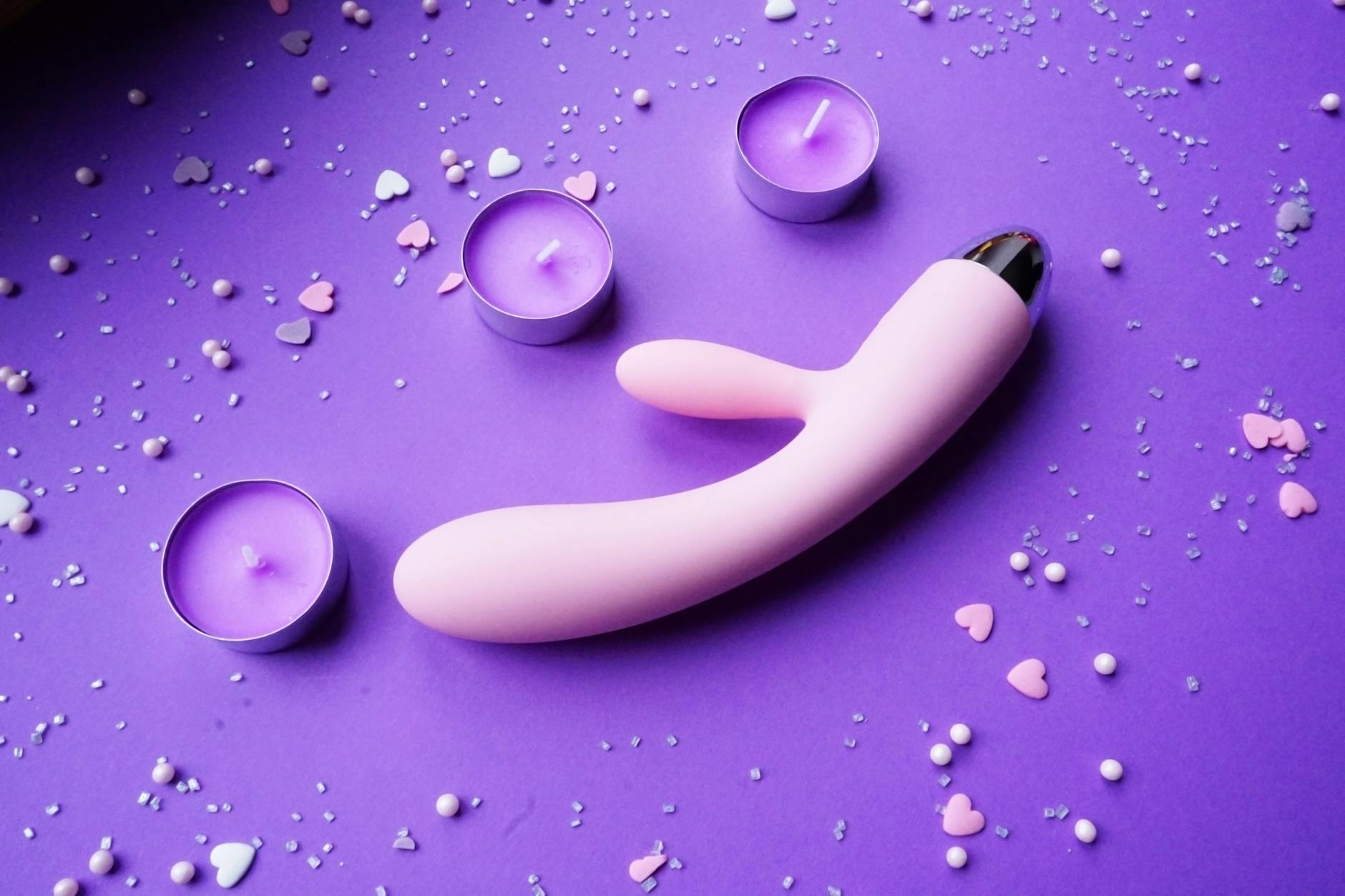 A pink clitoral vibrator on a purple surface with soft candlelight and flowers for a welcoming, pressure-free setup.